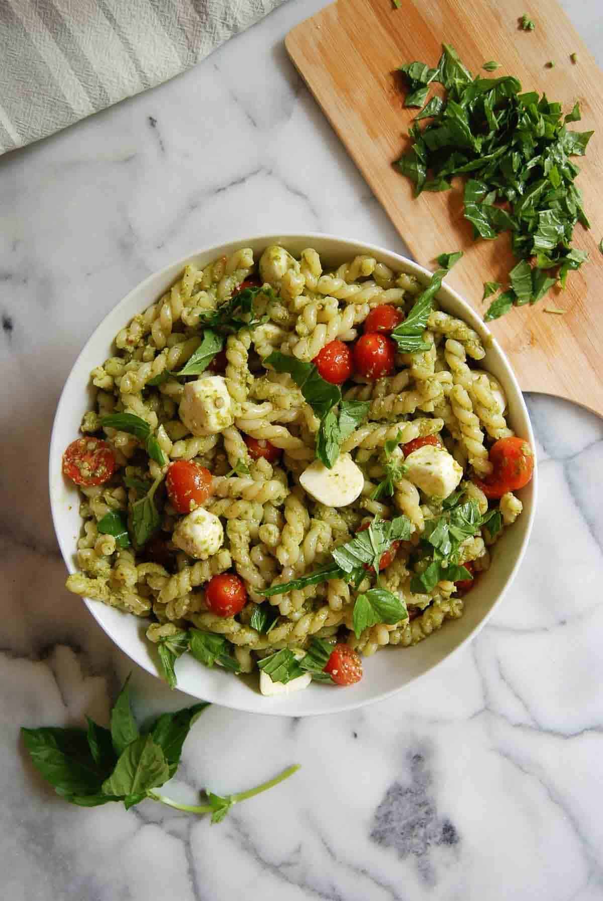 4-ingredient pesto pasta salad in serving bowl on countertop with basil sprinkled on top.