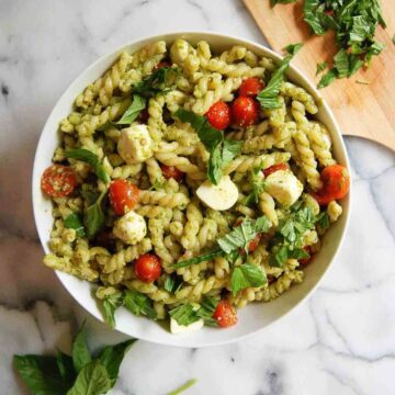 4-ingredient pesto pasta salad in serving bowl on countertop with basil sprinkled on top.