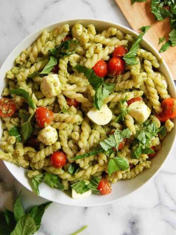 4-ingredient pesto pasta salad in serving bowl on countertop with basil sprinkled on top.