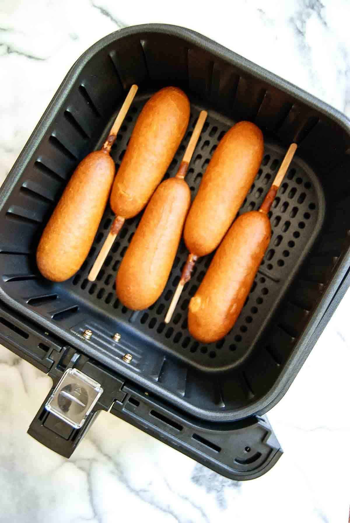 cooked corn dogs in air fryer basket.