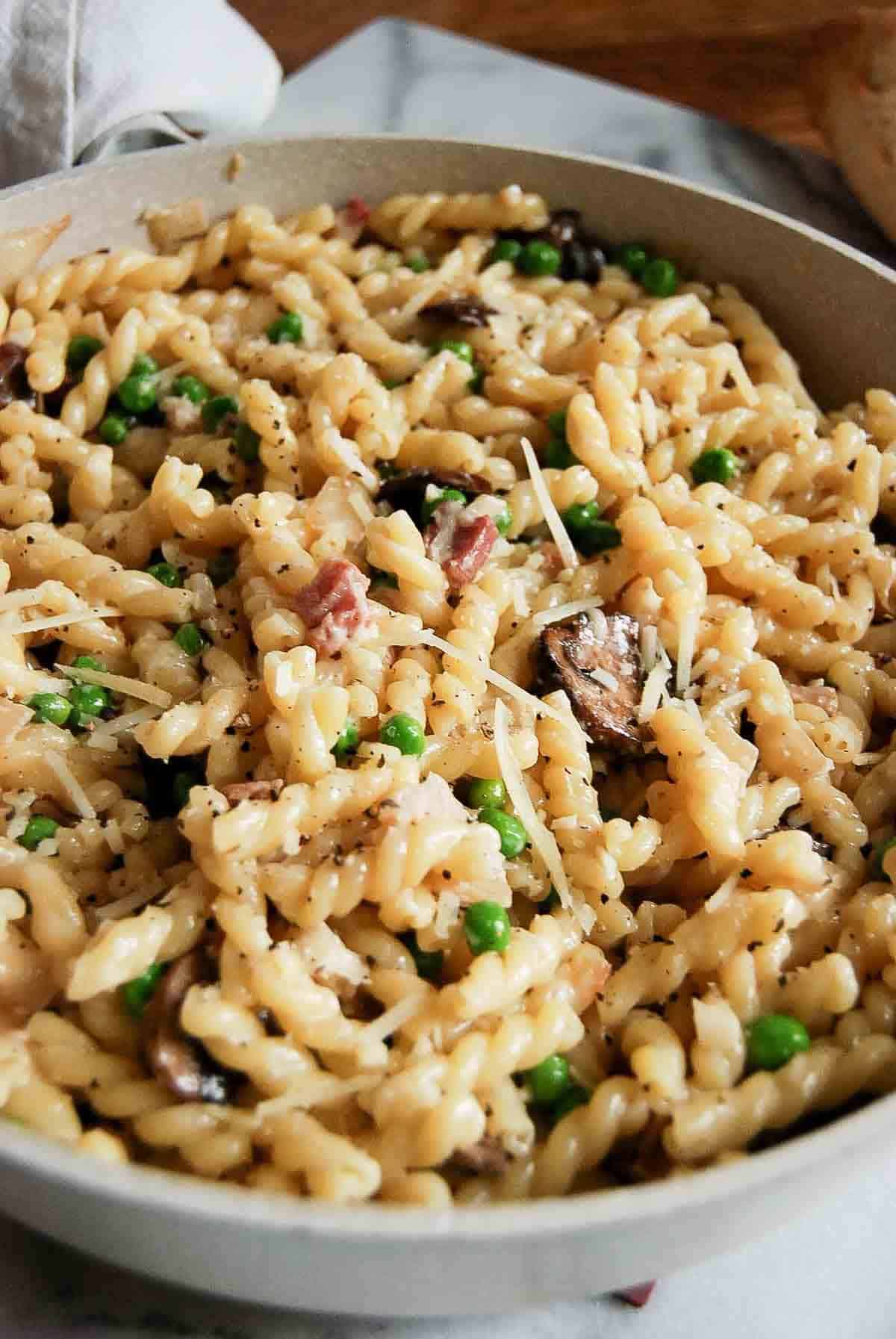 pasta with peas and pancetta in pan with loaf of crusty bread on the side.