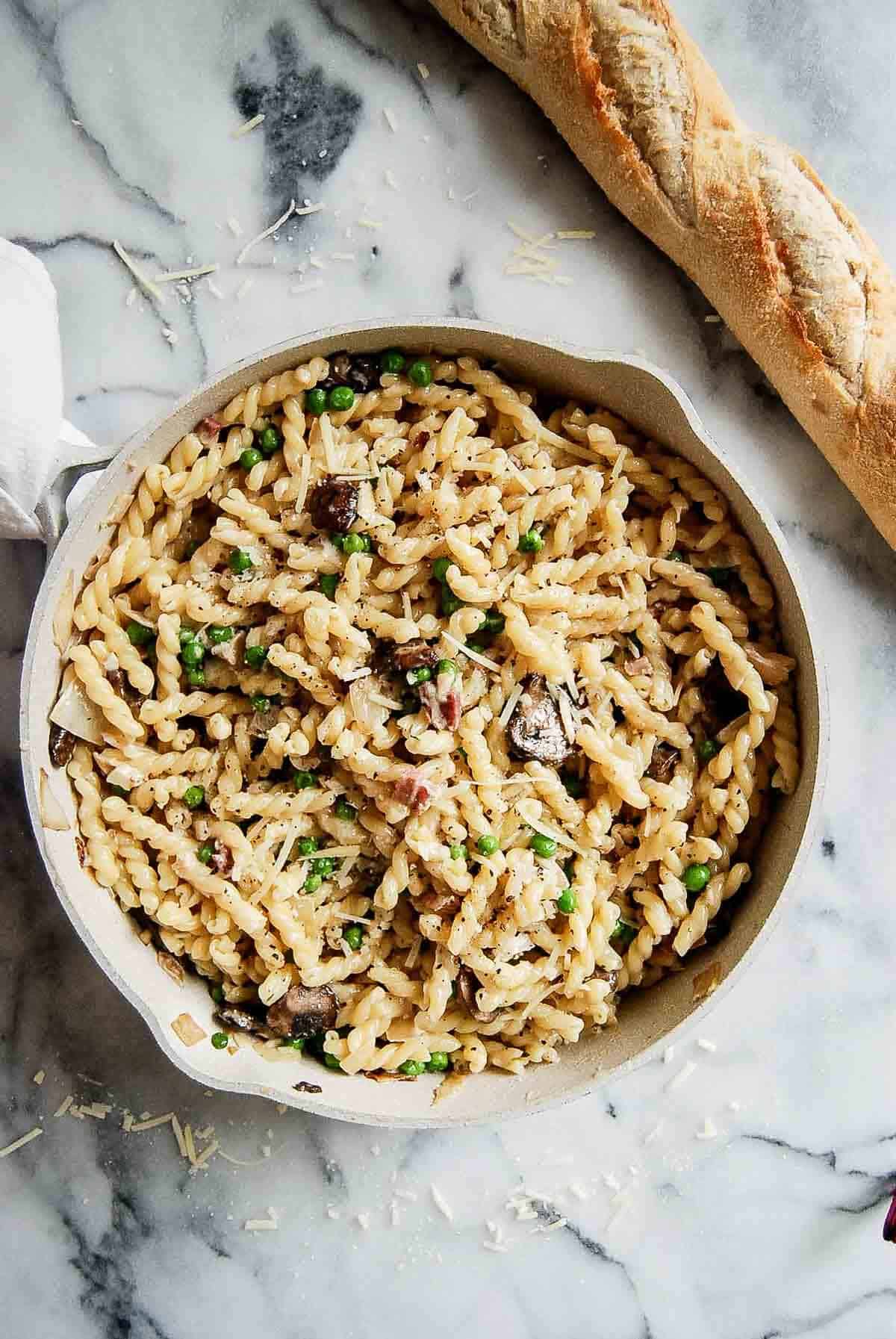 pasta with peas and pancetta in pan with loaf of crusty bread on the side.