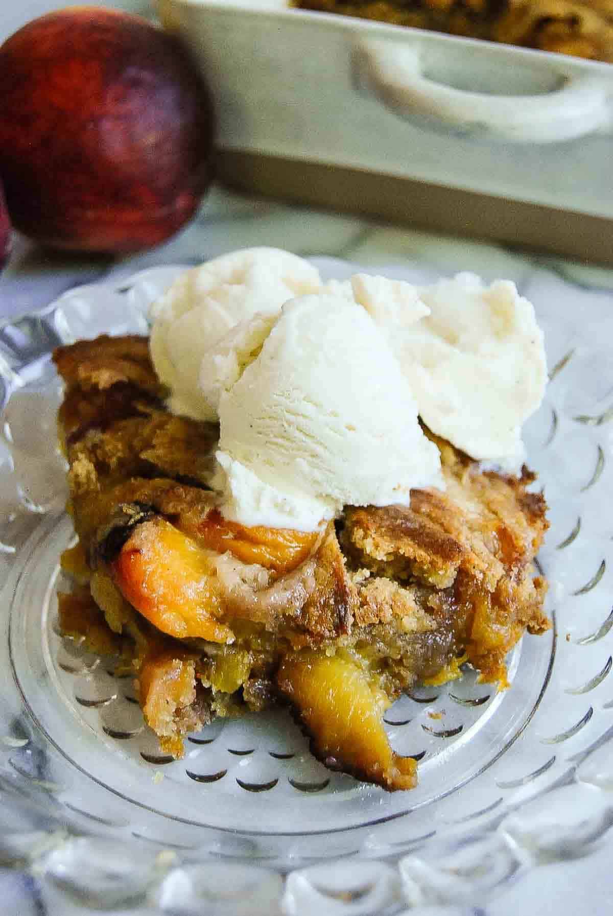 slice of peach cobbler, made from cake mix, on plate with a scoop of vanilla ice cream on top.