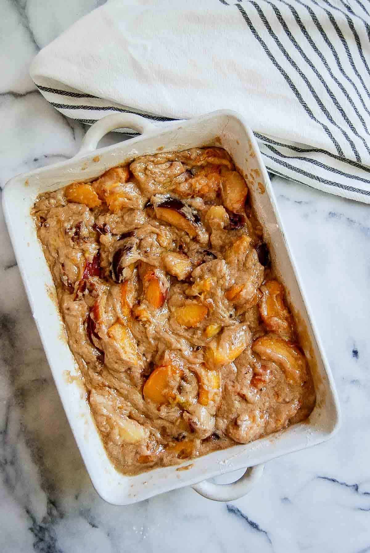 mixed cake batter and peaches in casserole dish.