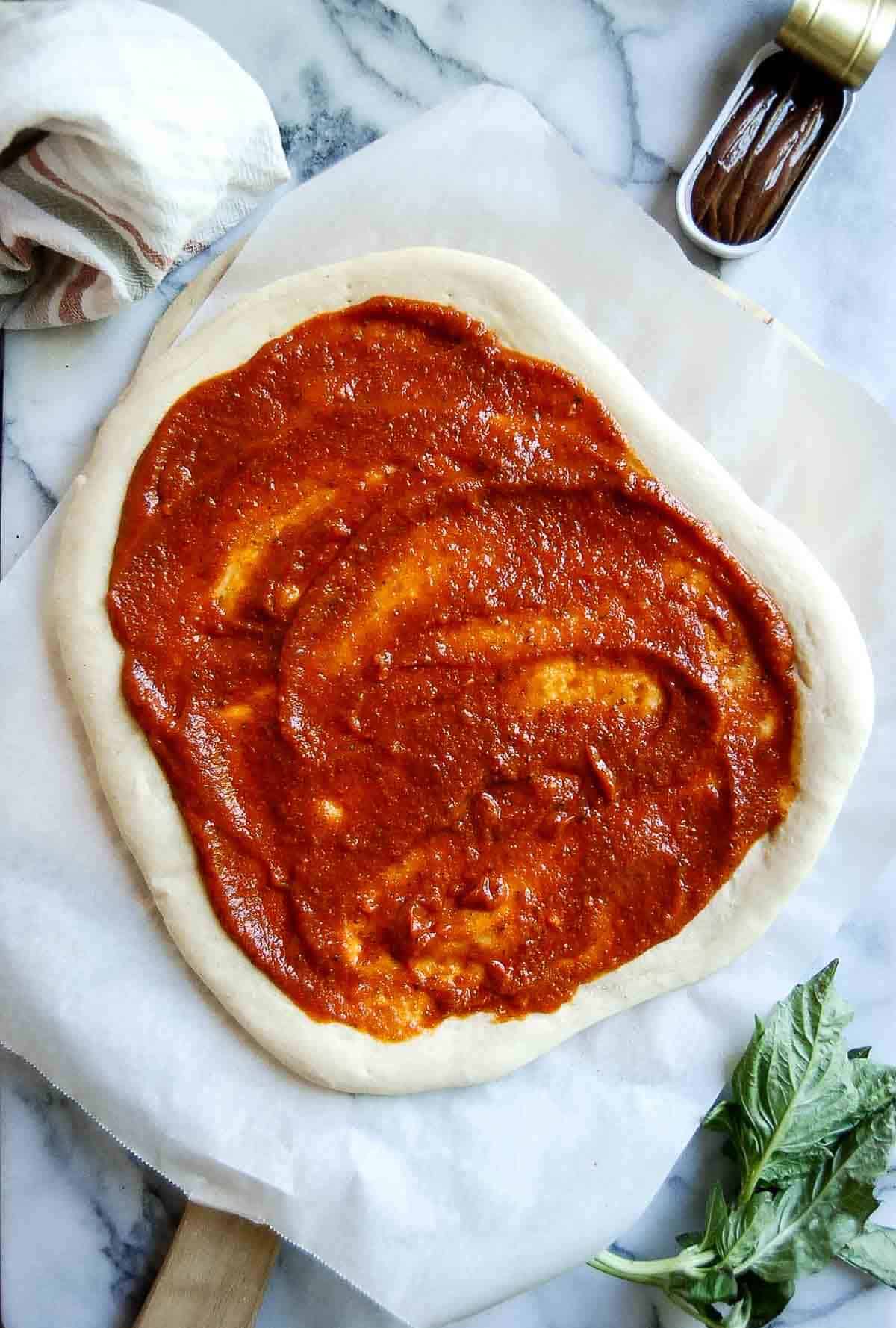 par baked pizza dough with red sauce spread on the top.