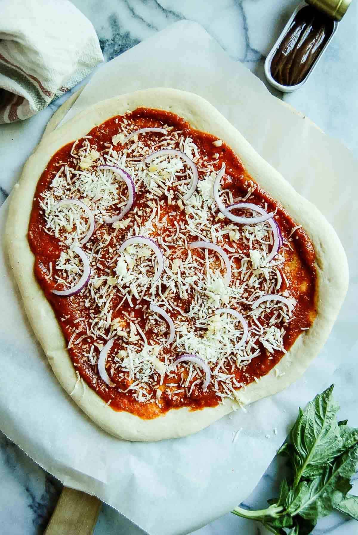 pizza dough with red sauce, cheese and red onions.