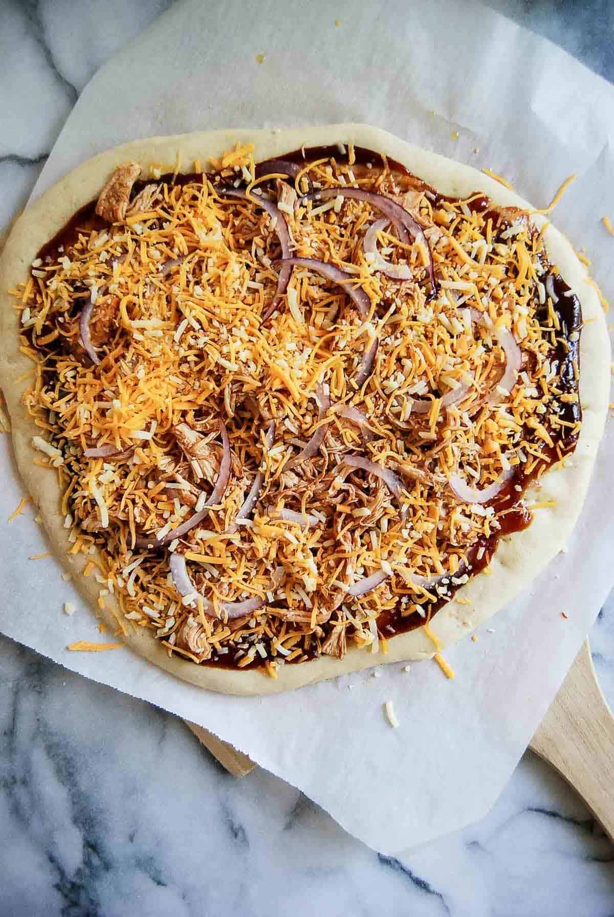 flatbread pizza with bbq sauce, cheese, chicken and red onion, before baking.