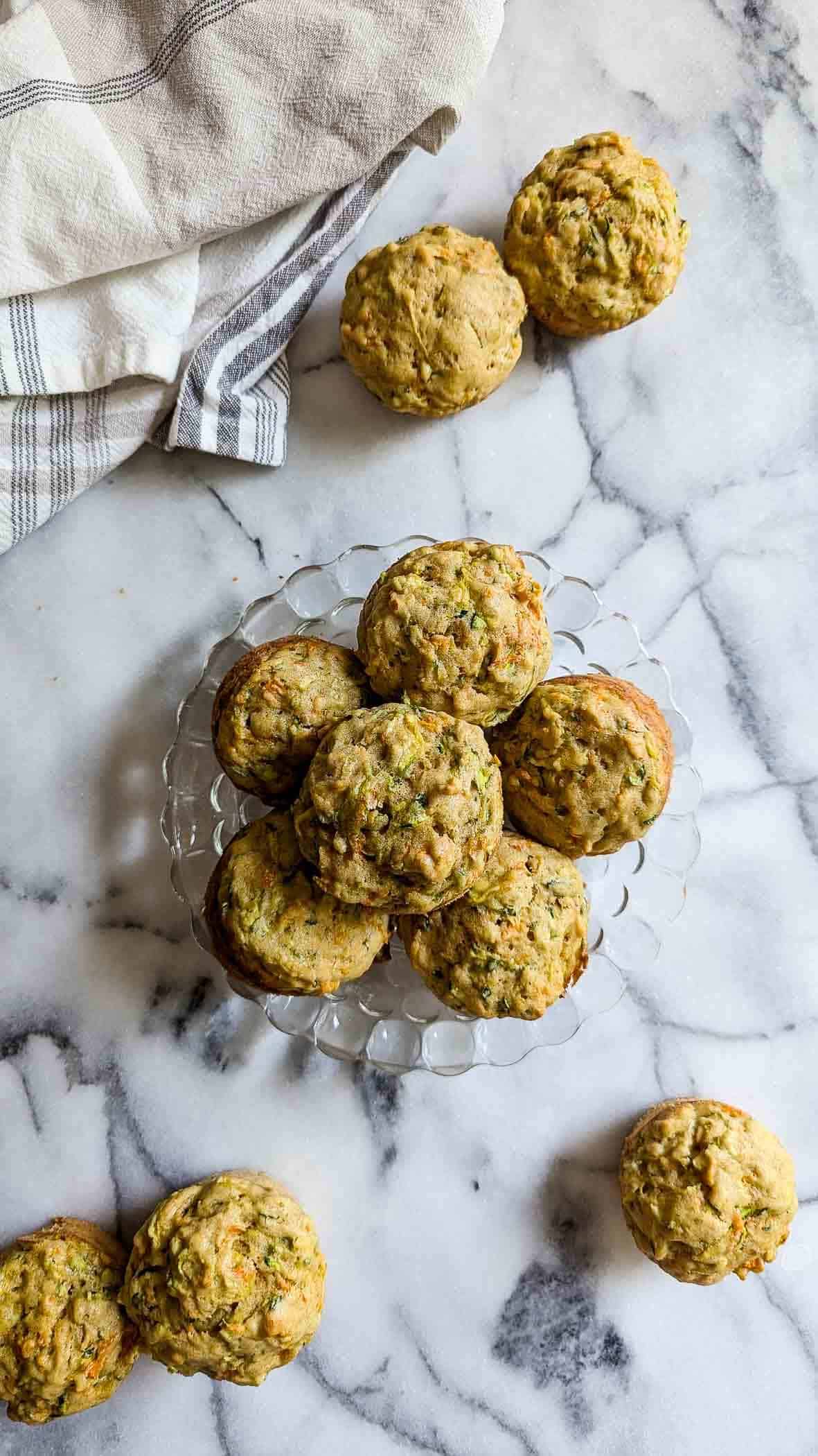 baked carrot zucchini muffins on plate, with others scattered on countertop.