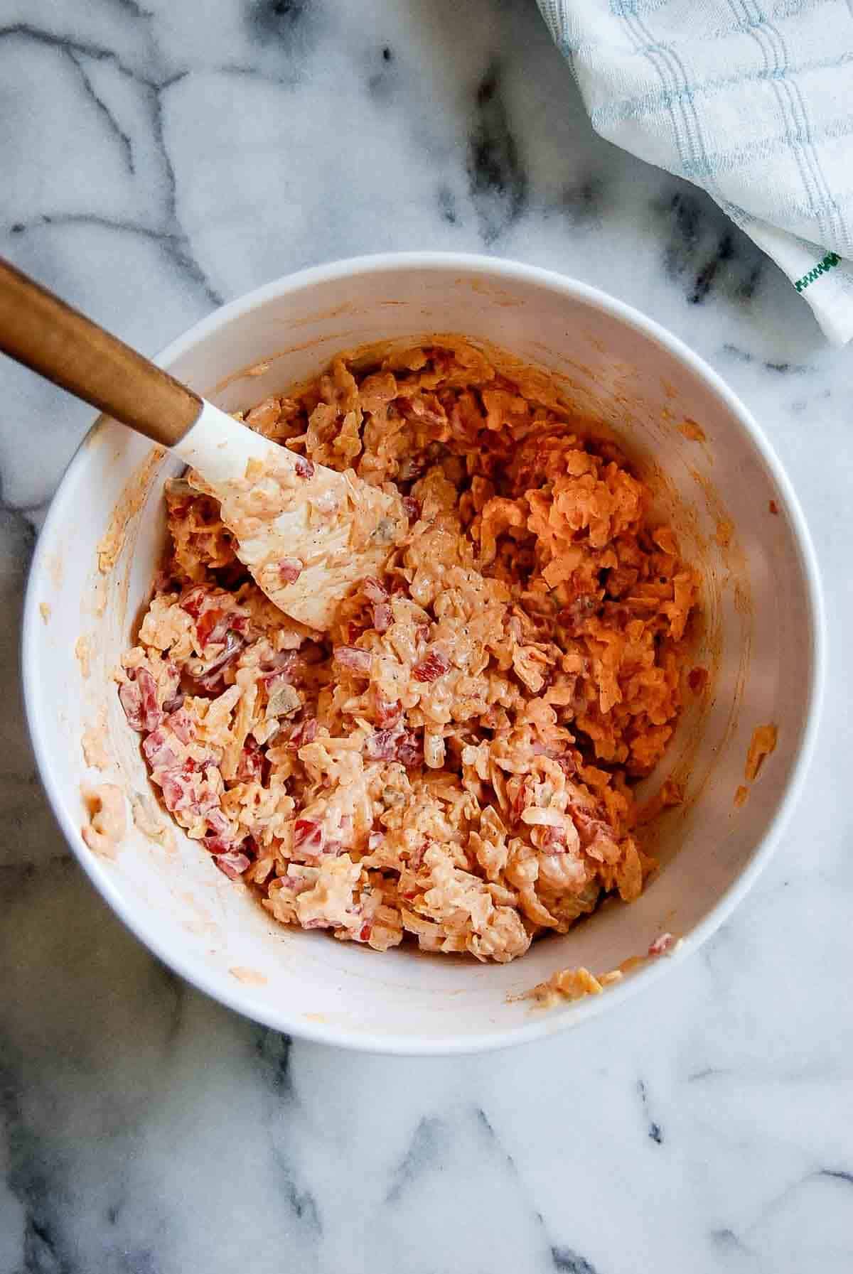 shredded sharp cheddar, pimento peppers and mayonnaise in a mixing bowl with a spatula.