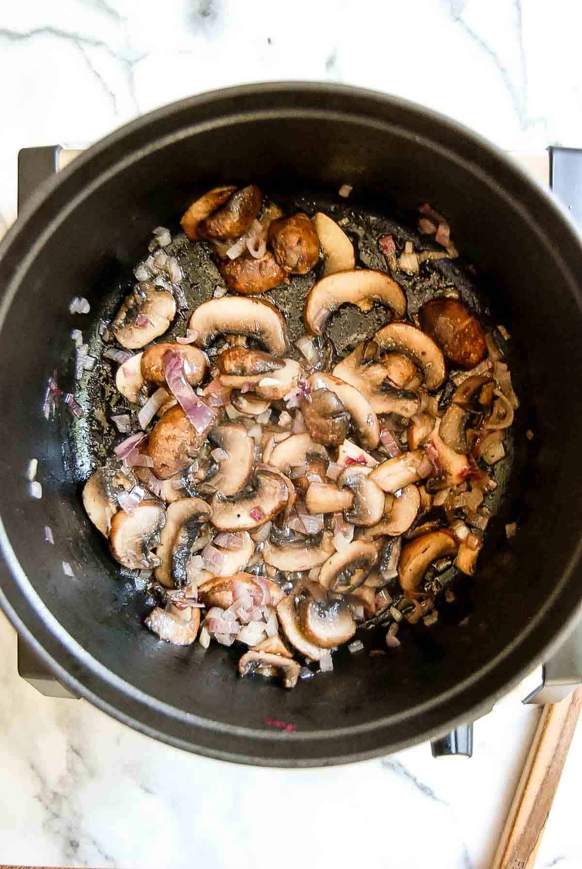 mushrooms and shallots sautéing in pot.