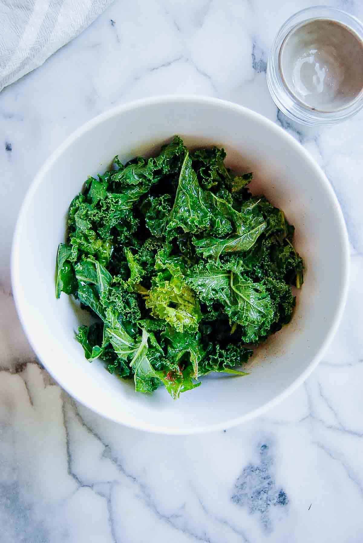 kale pieces massaged with oil and seasoned, in bowl.