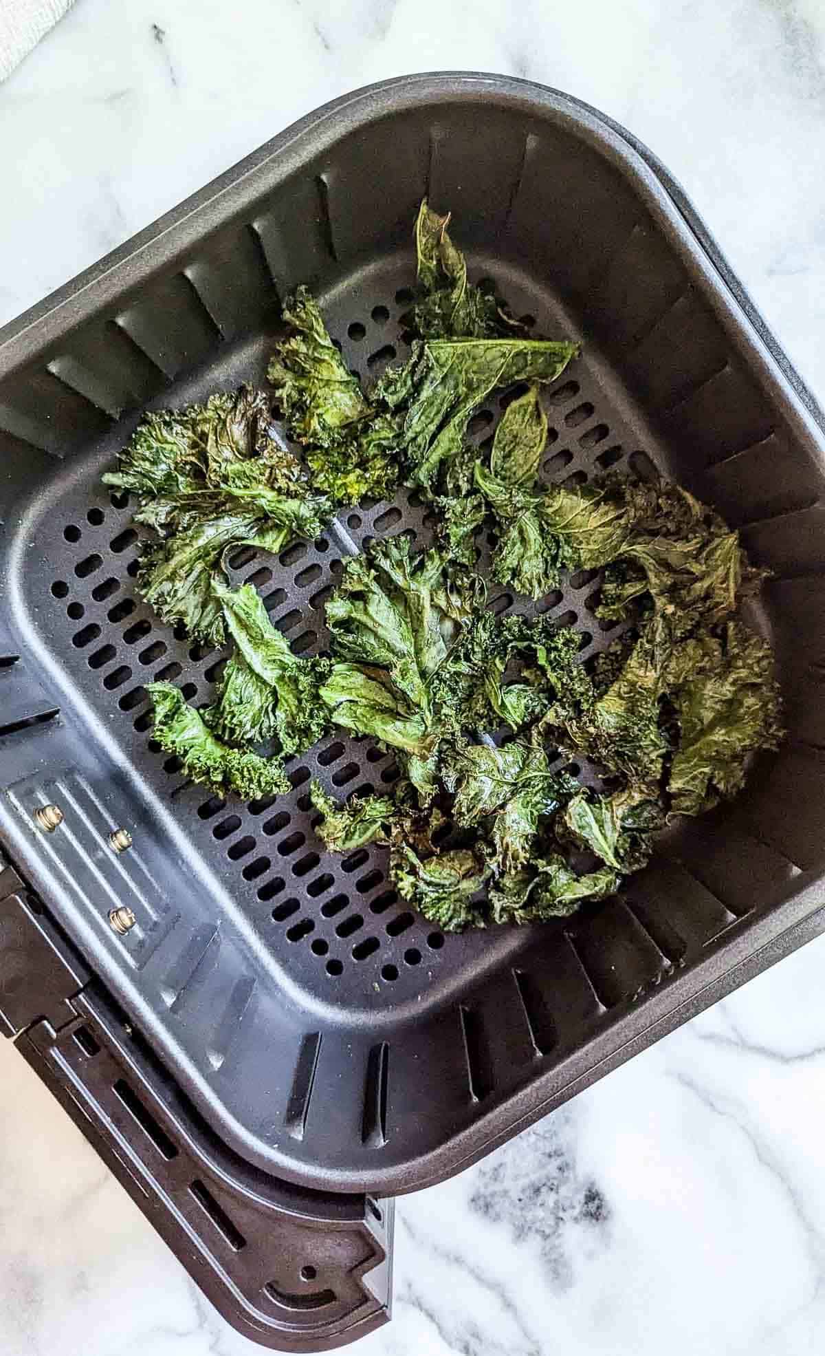 cooked air fryer kale chips in air fryer basket.