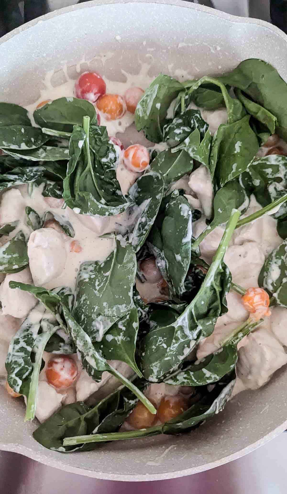 chicken, tomatoes and spinach in Boursin cheese sauce in pan.