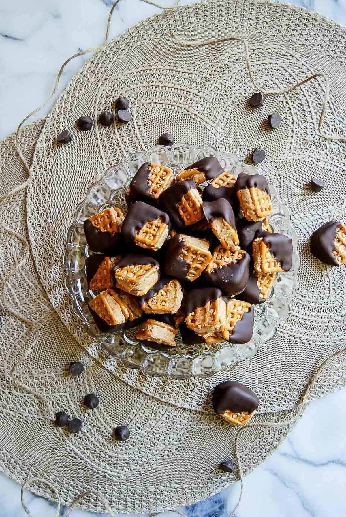 bowl of chocolate dipped peanut butter pretzel bits in bowl on countertop with chocolate chips scattered around the bowl.