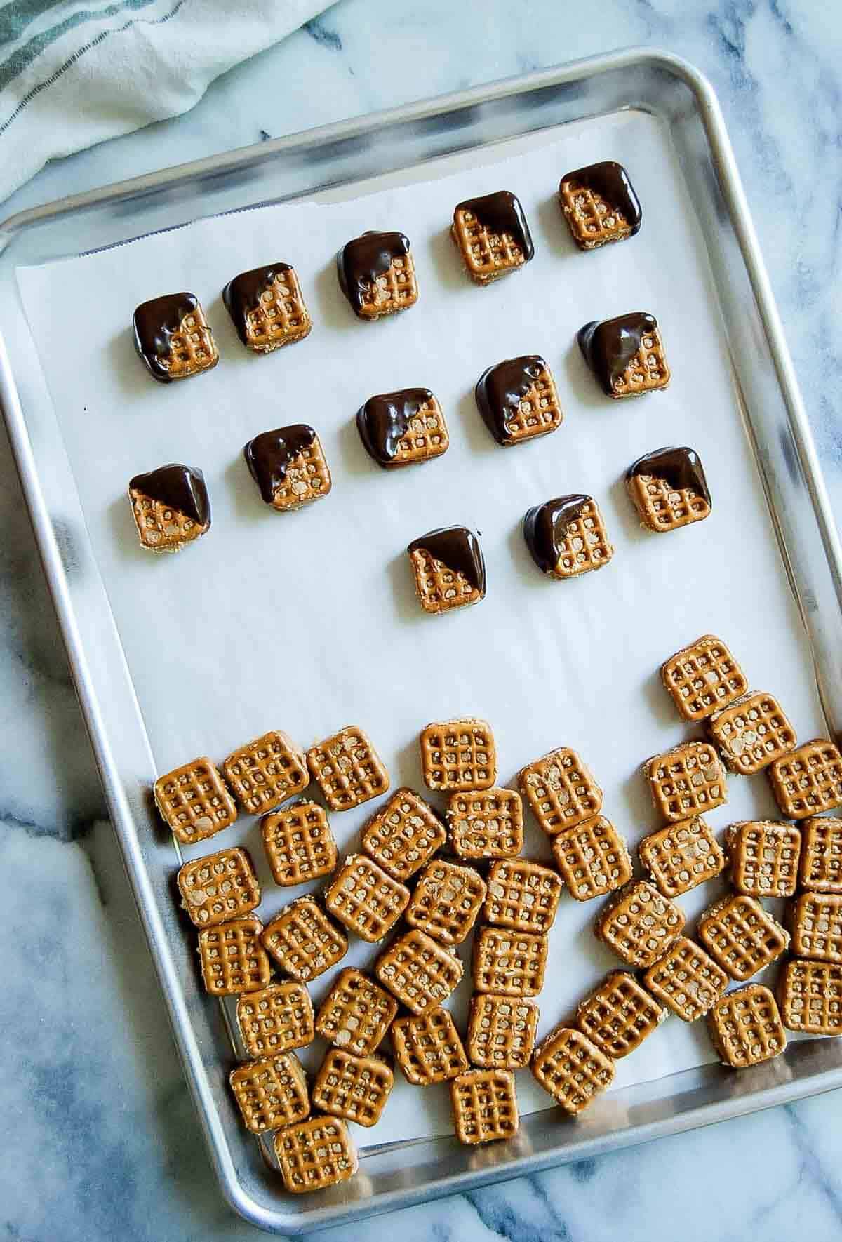 peanut butter pretzel bites on baking tray, half dipped in chocolate.