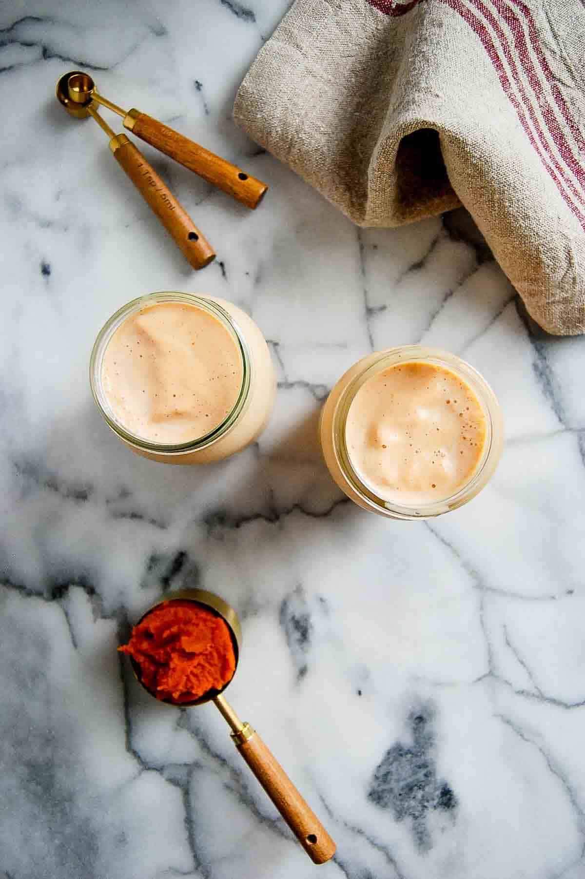two glasses filled with pumpkin spice frosty on countertop with scoop of pumpkin puree on the side.