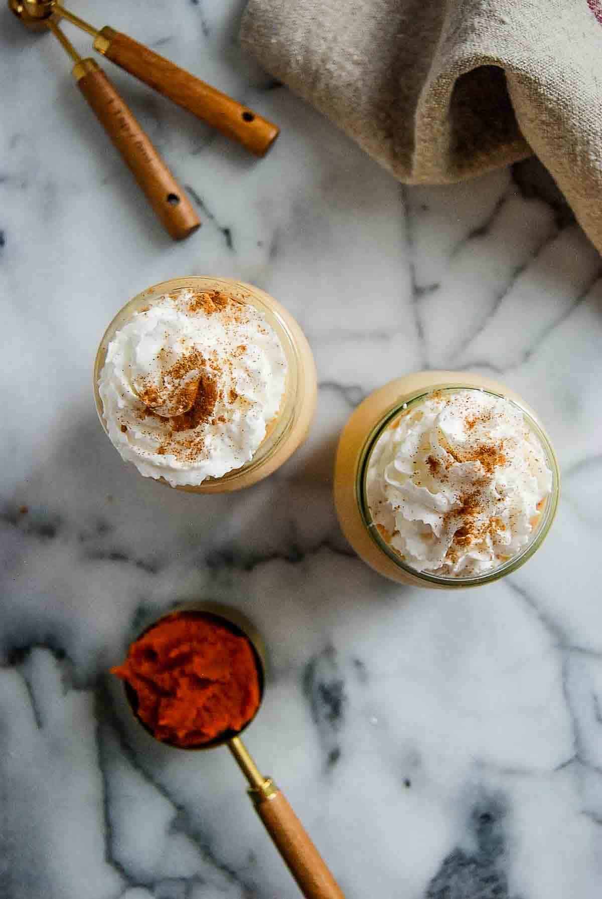 two glasses filled with pumpkin spice frosty on countertop with scoop of pumpkin puree on the side.
