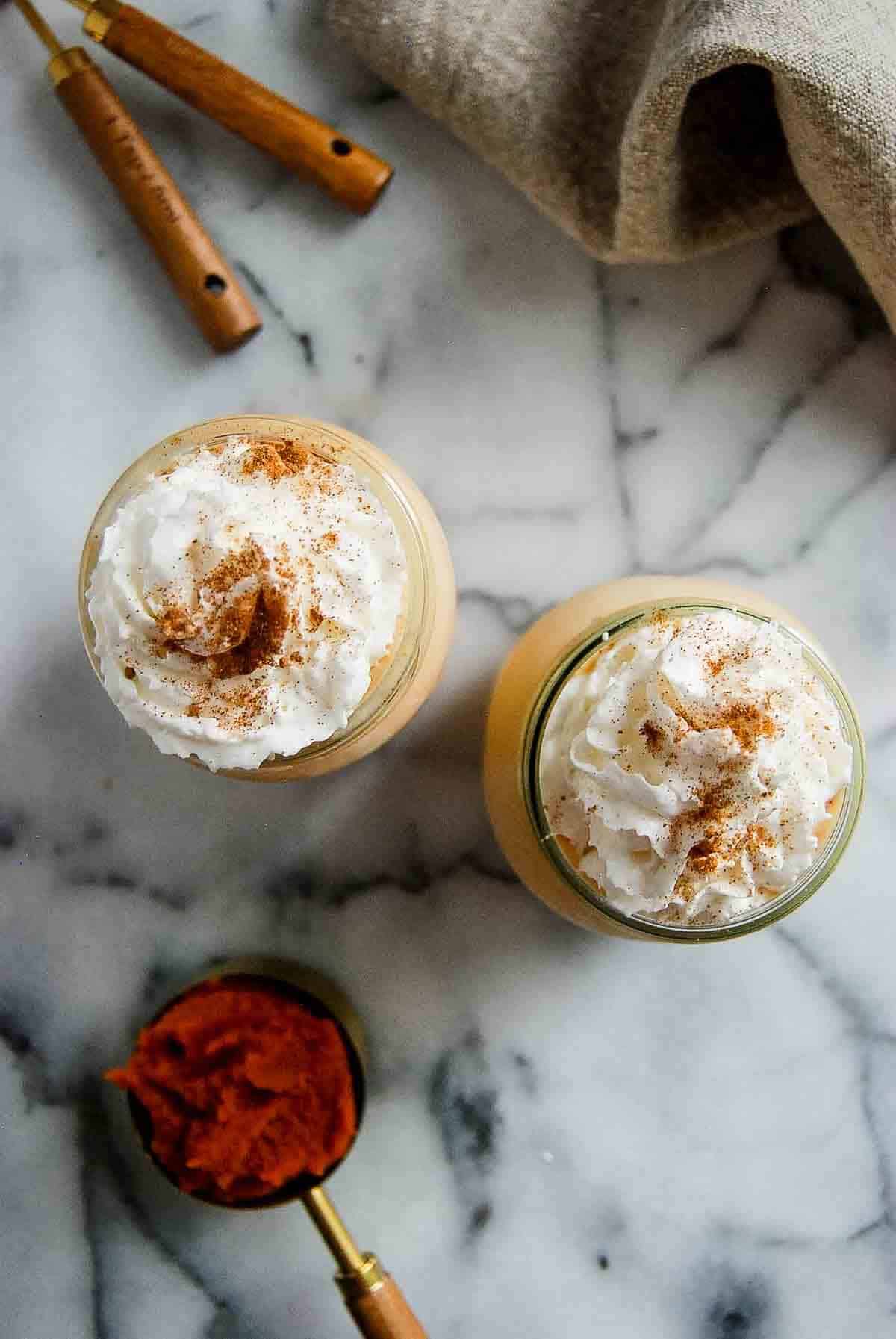 two glasses filled with pumpkin spice frosty on countertop with scoop of pumpkin puree on the side.