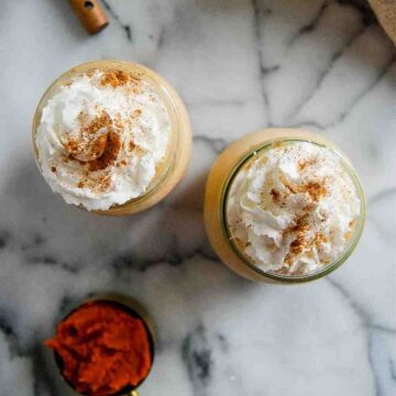 two glasses of pumpkin spice frosty on countertop with scoop of pumpkin puree on the side.