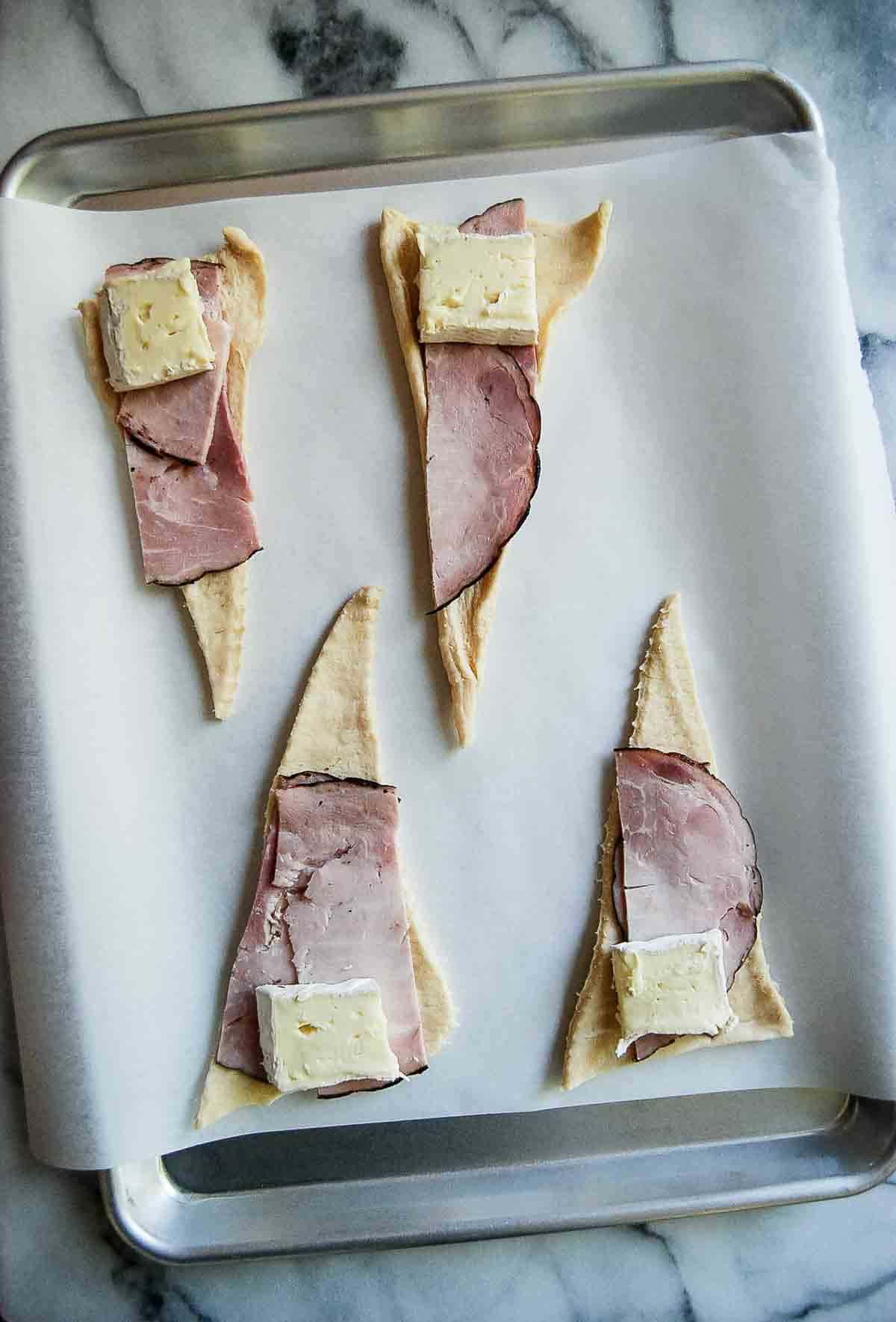 rolled out crescent rolls with ham slices and brie cheese on top.