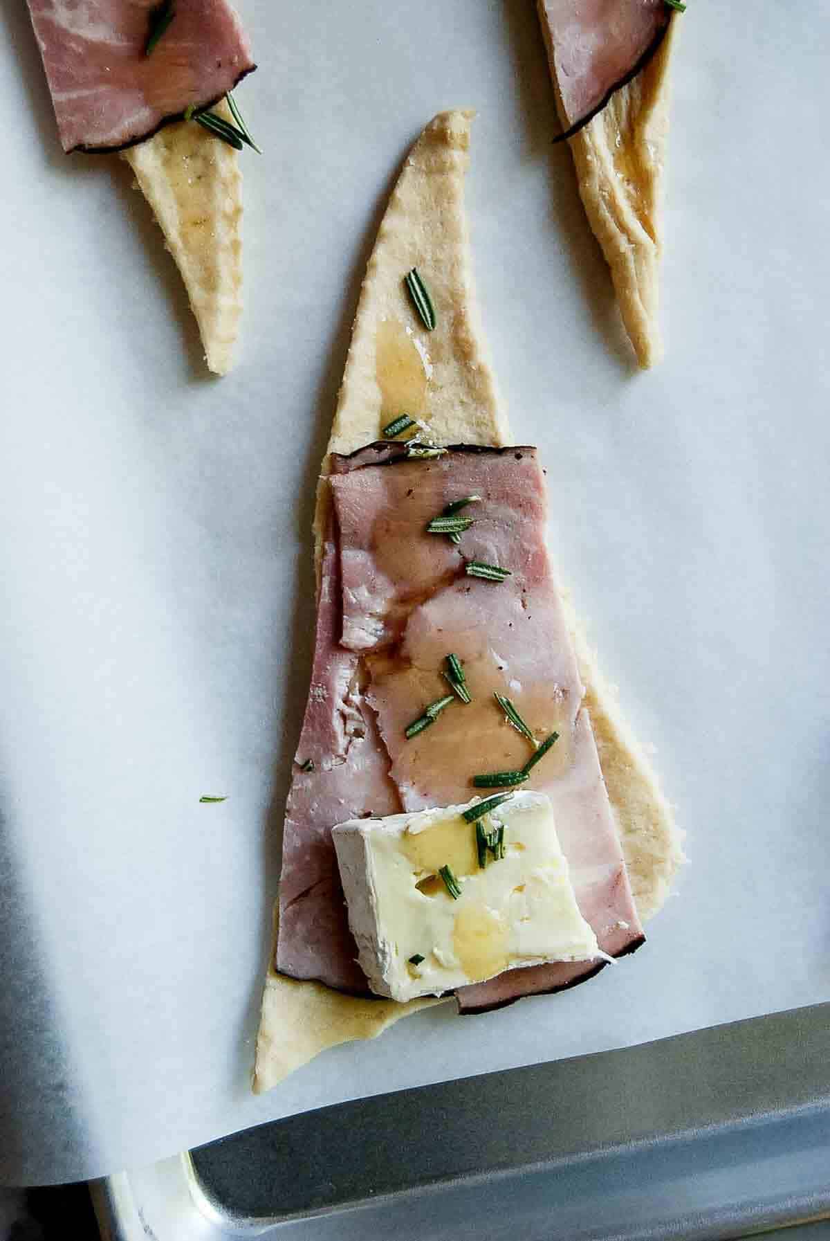 closeup of crescent roll dough with ham, cheese, rosemary and honey.