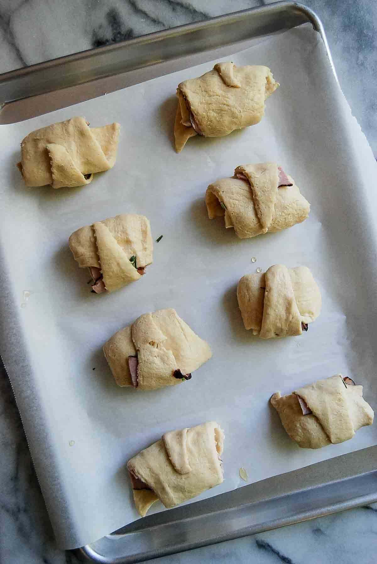 rolled up ham and cheese crescent rolls on tray ready for baking.