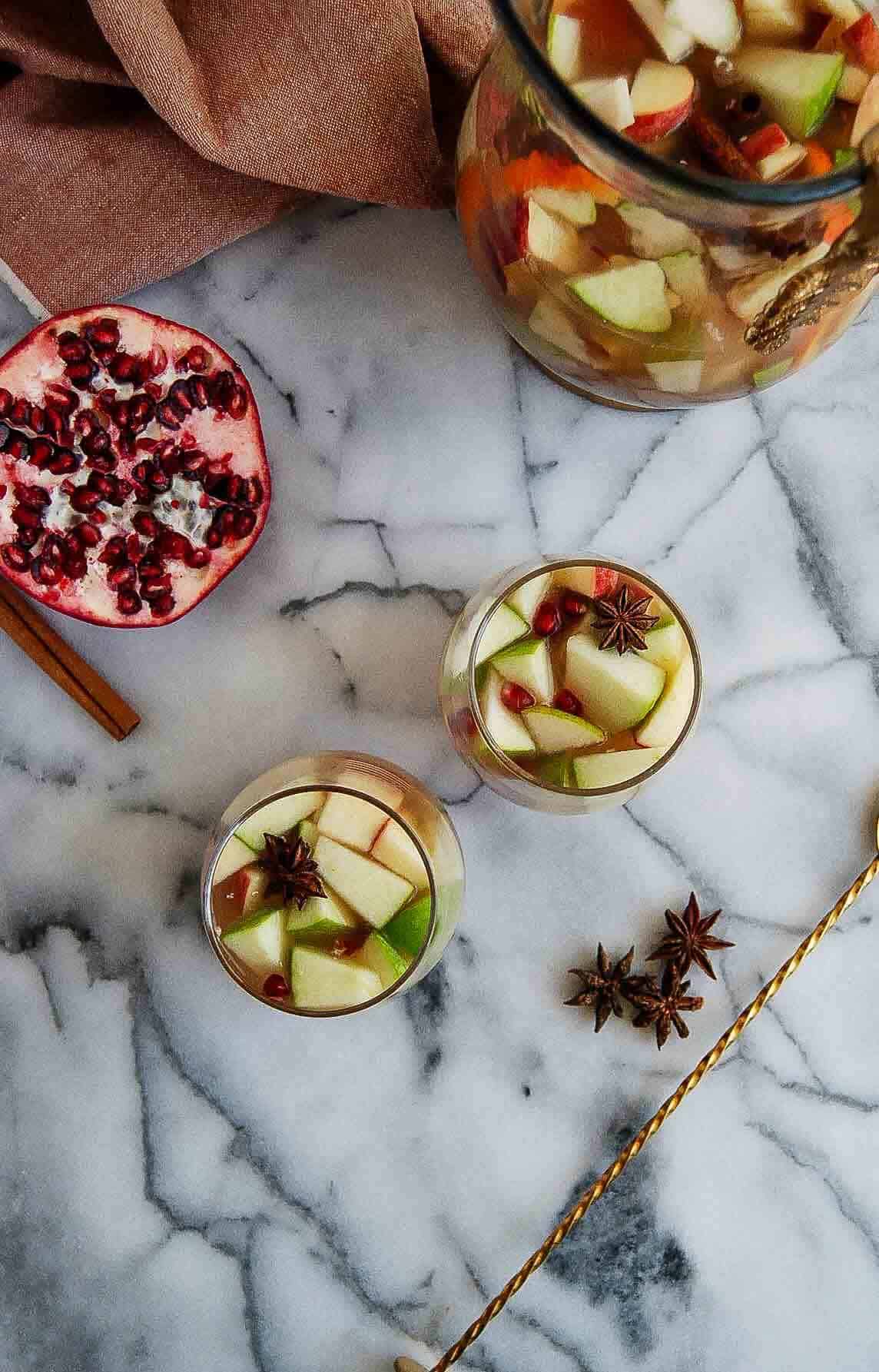 two glasses of thanksgiving sangria on countertop with stirrer and pomegranate on the side.