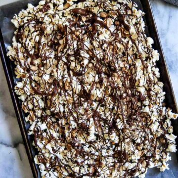 sheet pan of chocolate drizzled popcorn with peanuts.
