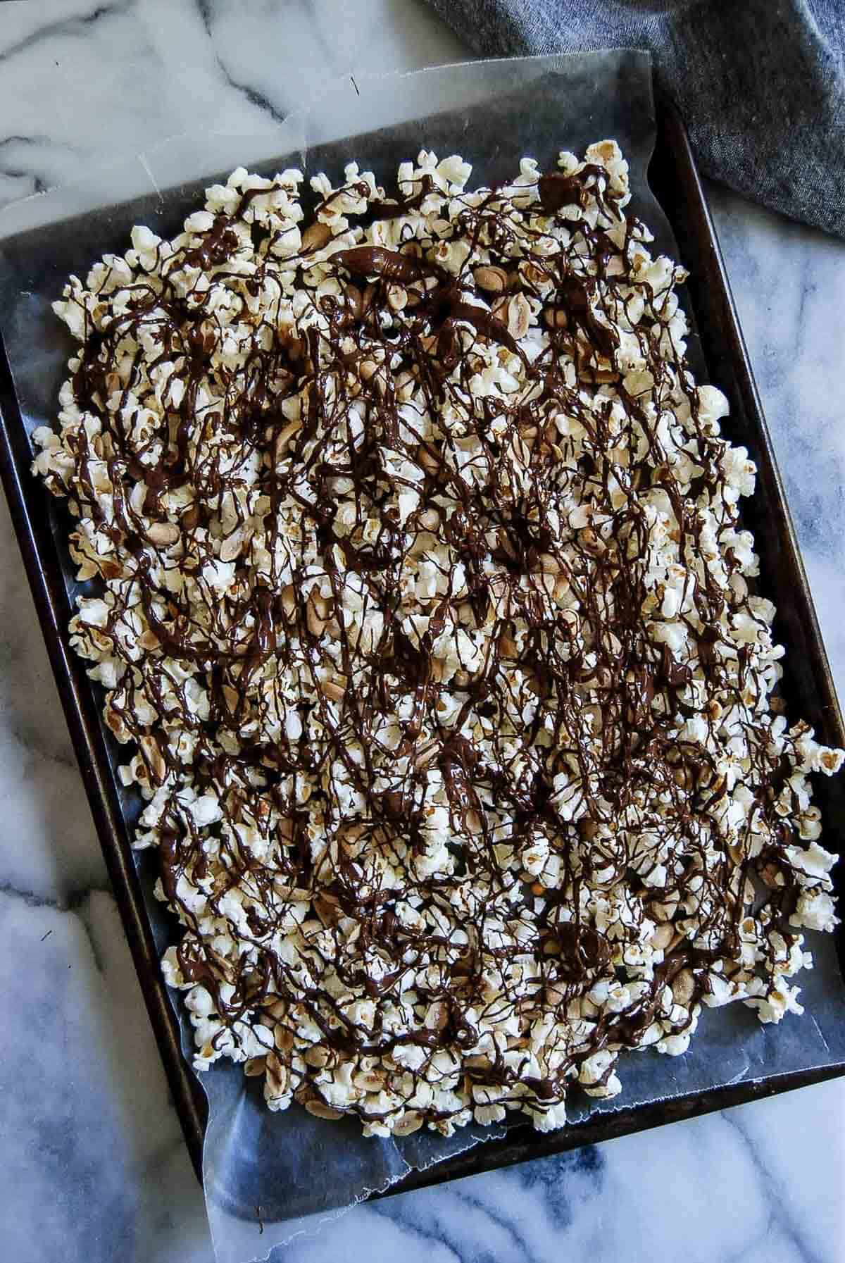 chocolate drizzled popcorn with peanuts on sheet pan.