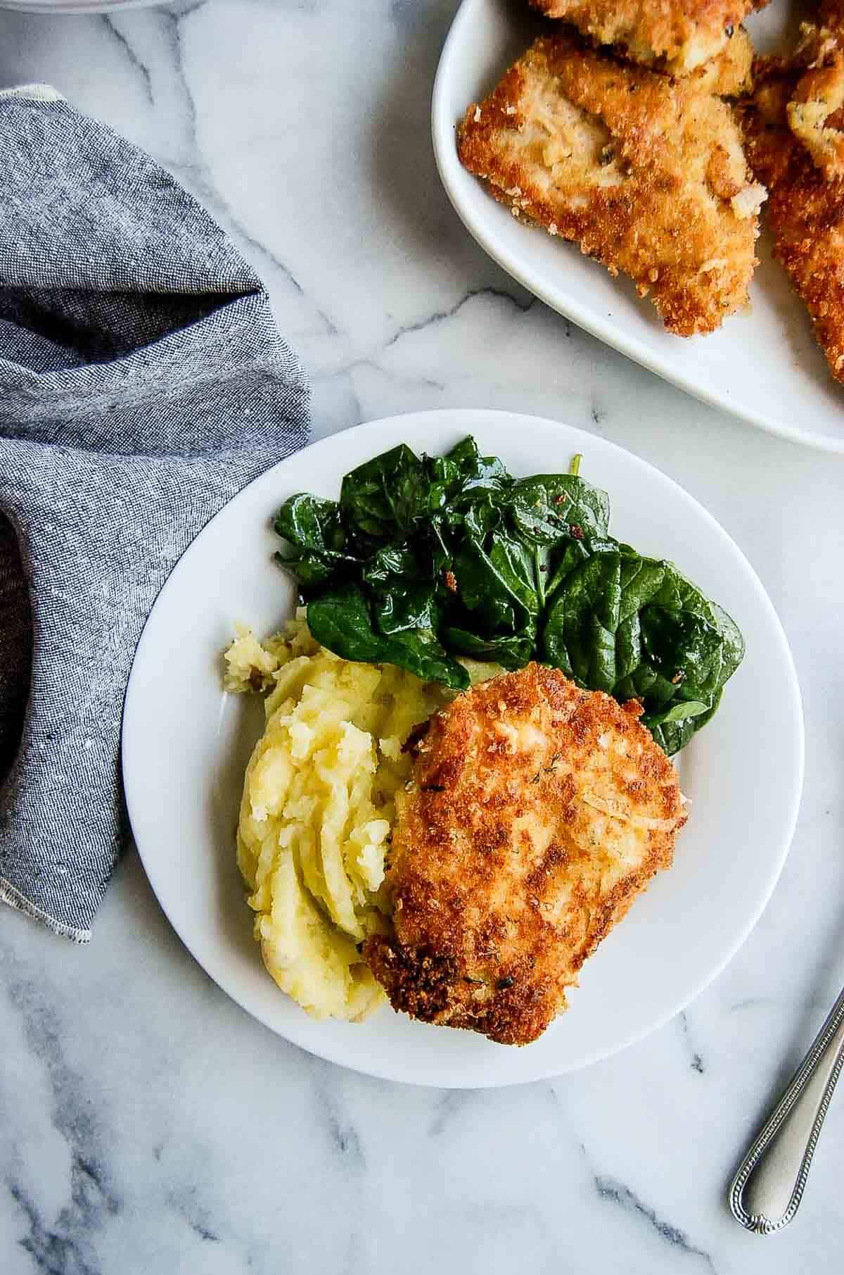 crispy chicken fritta on plate with mashed potatoes and cooked spinach.