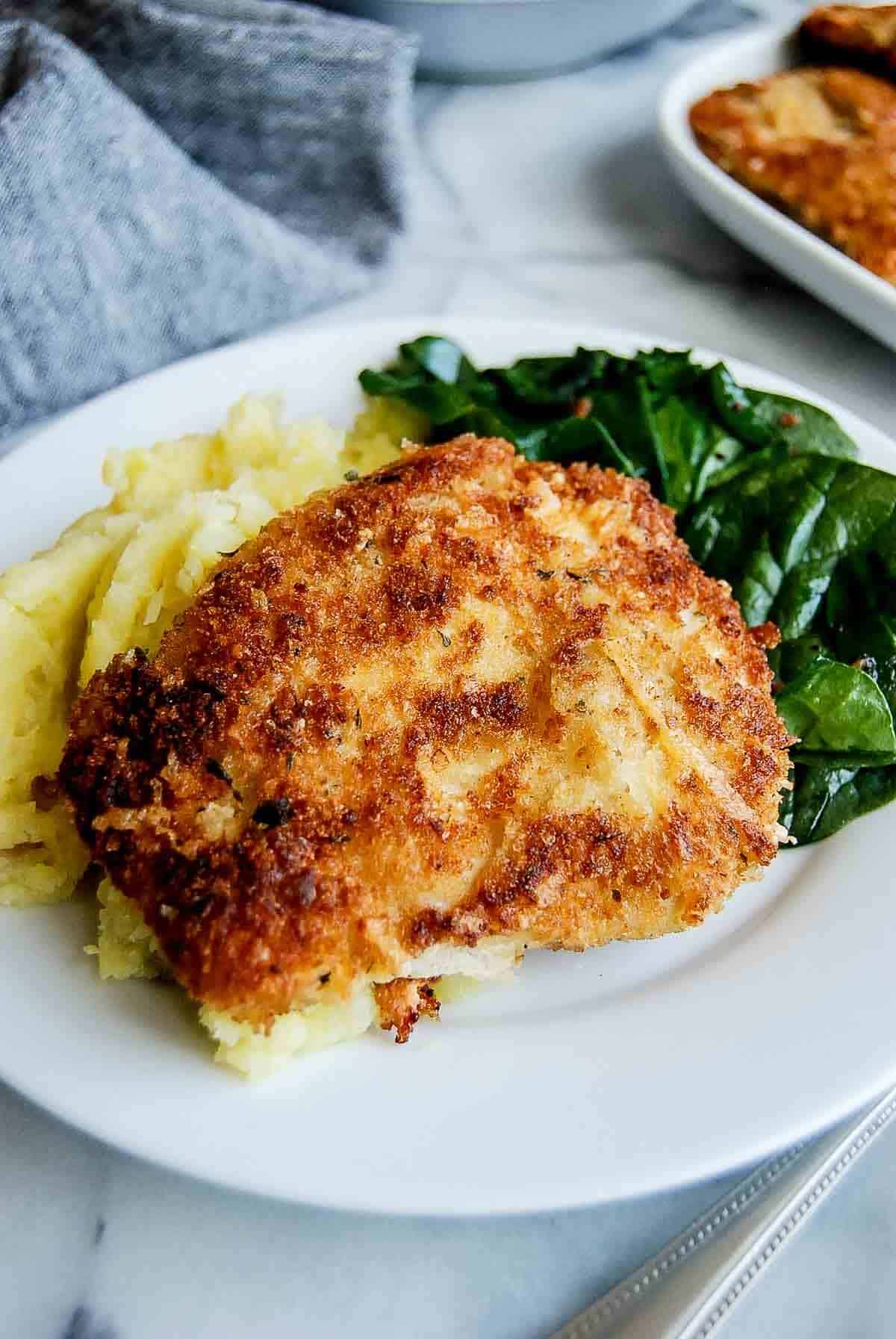 crispy chicken fritta on plate with mashed potatoes and cooked spinach.