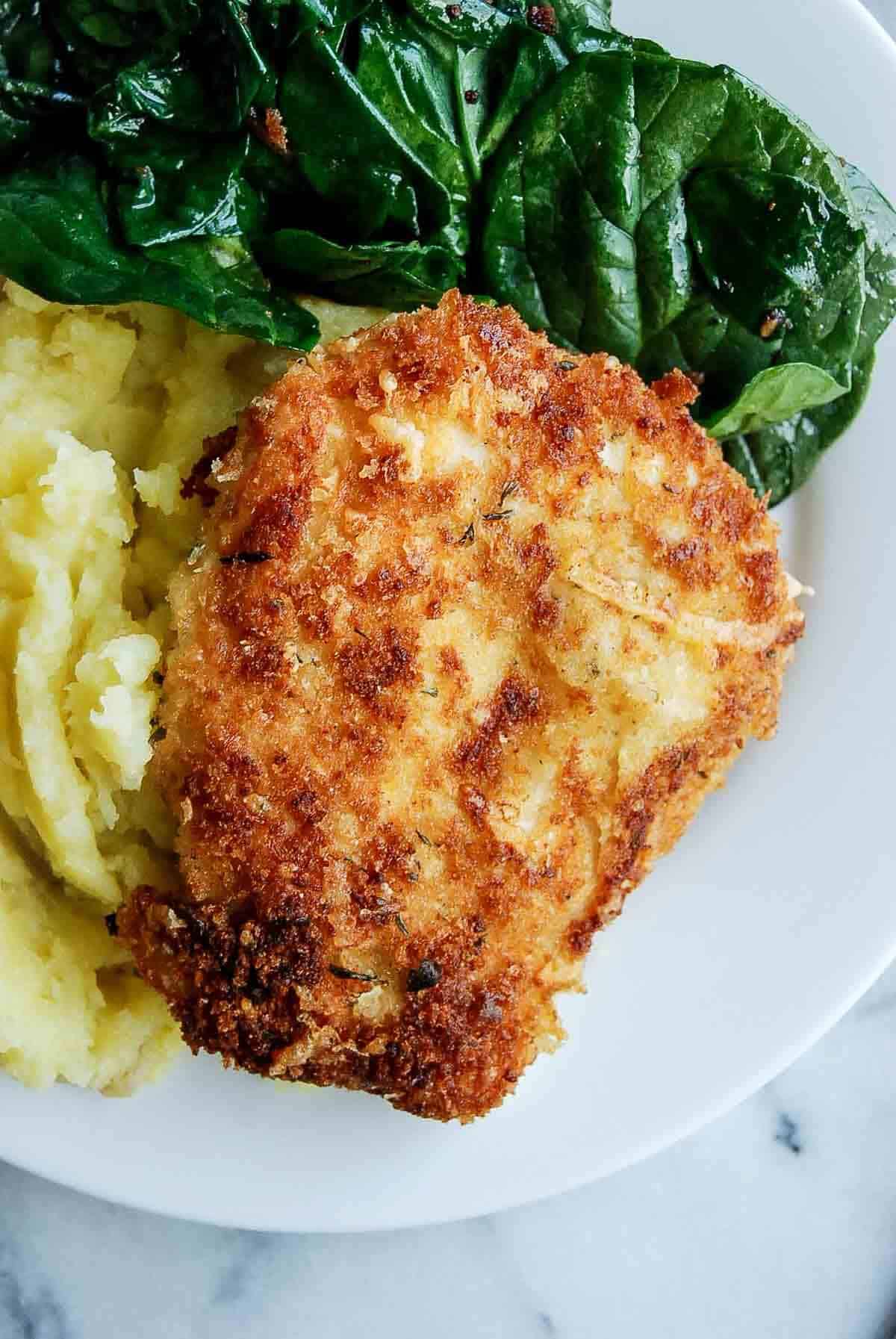 crispy chicken fritta on plate with mashed potatoes and cooked spinach.