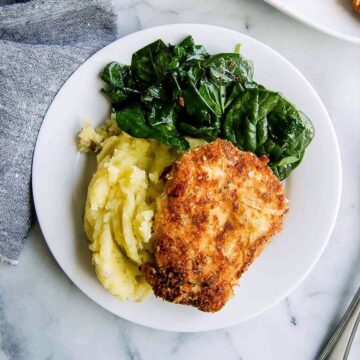 crispy chicken fritta on plate with mashed potatoes and cooked spinach.