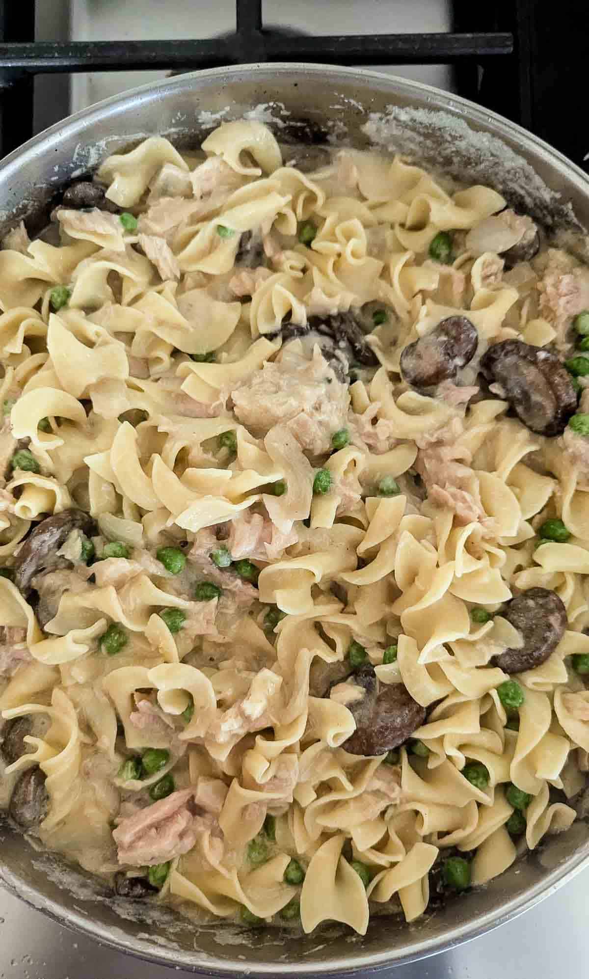 tuna helper casserole with egg noodles, mushrooms and frozen peas in pan.