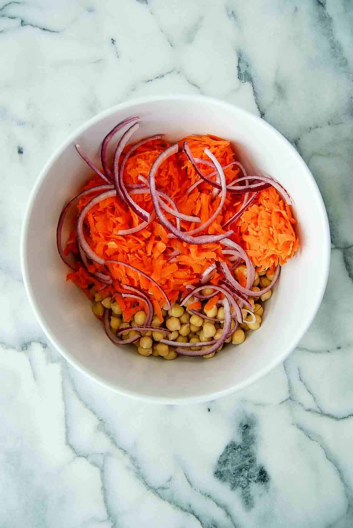 carrots, chickpeas, onions and dates in bowl on countertop.