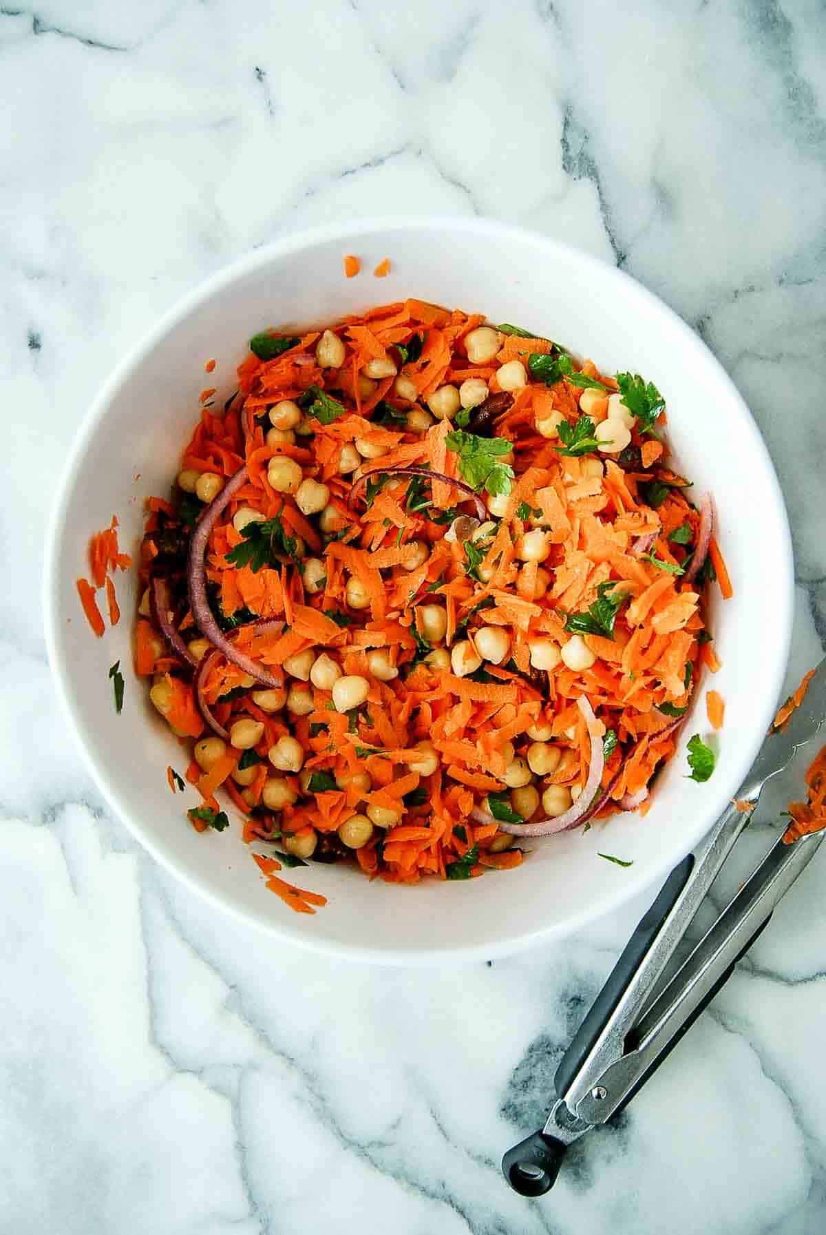 carrots, chickpeas, onions, dates and parsley mixed, in bowl on countertop.