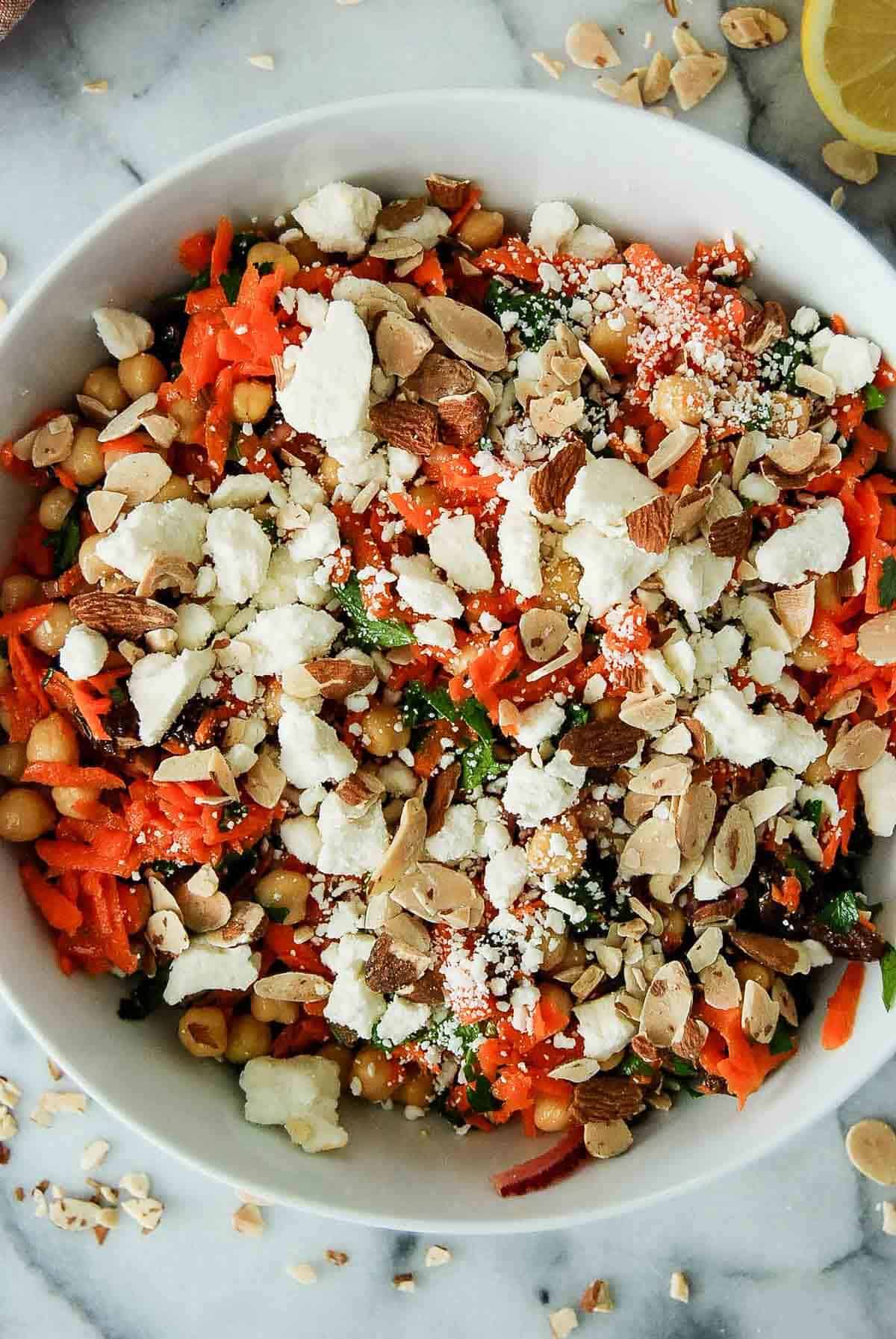 closeup of carrot and chickpea salad in bowl on countertop, with feta and sliced almonds sprinkled on top.