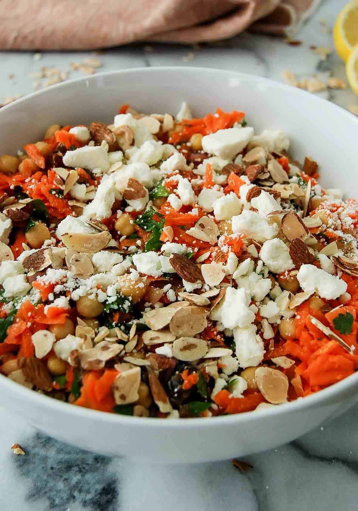 side view of carrot and chickpea salad in bowl on countertop, with feta and sliced almonds sprinkled on top.