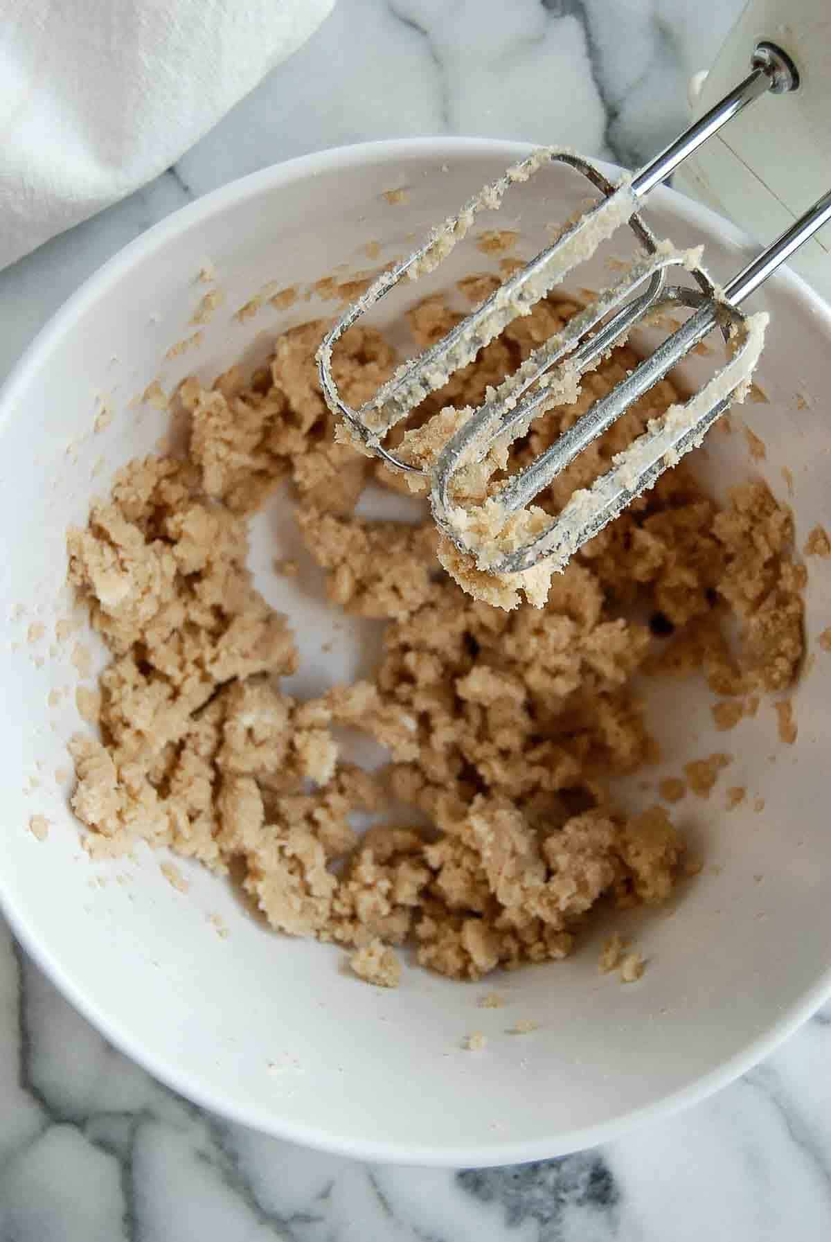 bowl with butter and sugars, creamed, with hand mixer on the side.