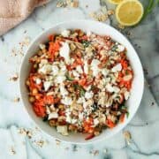 carrot and chickpea salad with lemon and parsley in bowl on countertop, with feta and sliced almonds sprinkled on top.