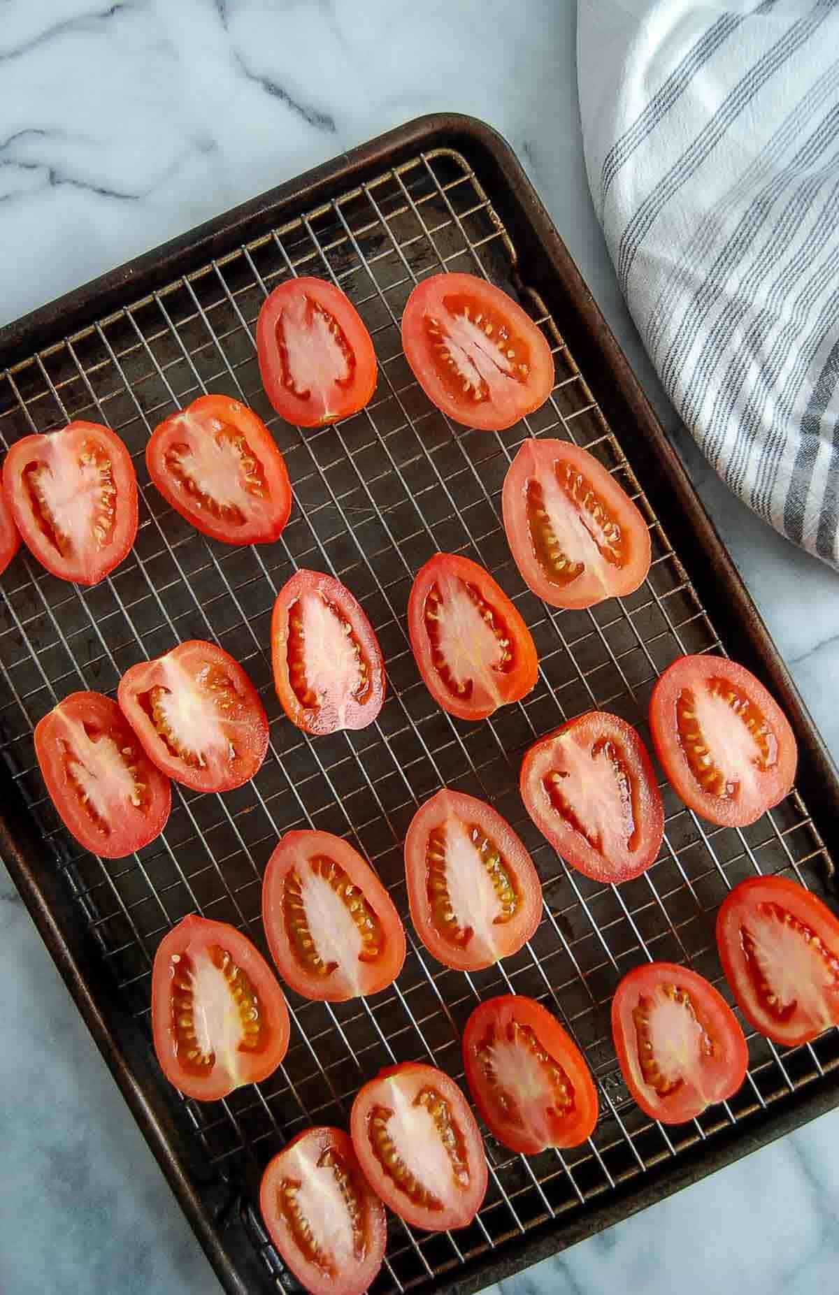 sliced roma tomatoes on pan lined with wire rack.