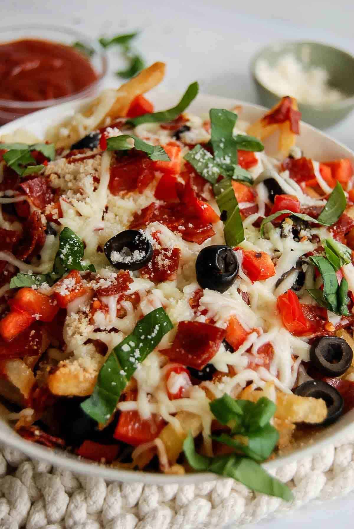 side view of loaded pizza fries with pepperoni, red pepper, black olives, mozzarella, and basil.