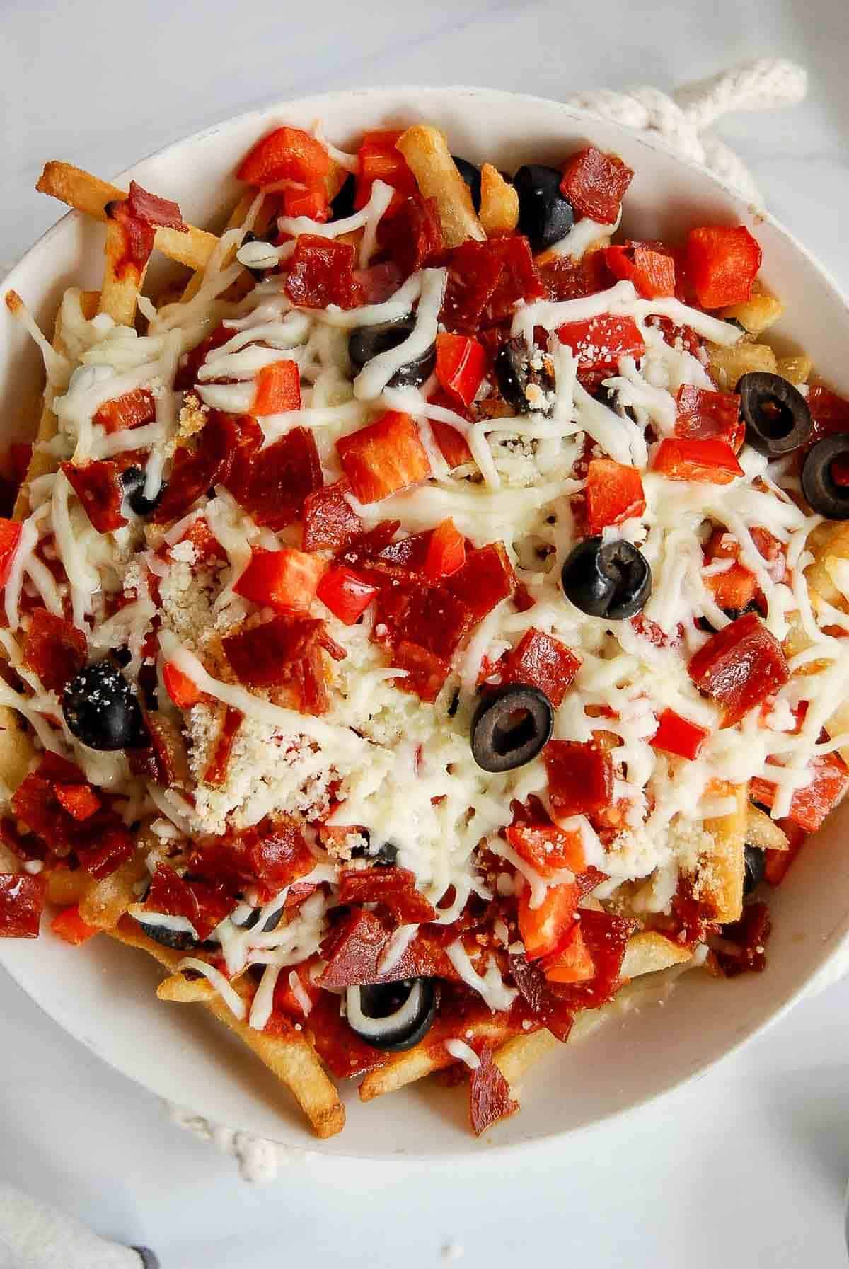 closeup of pizza fries with melted mozzarella, black olives, pepperoni and red pepper.