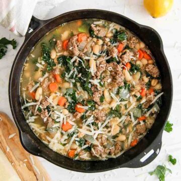 pot of sausage kale and white bean soup with shredded parmesan on top and lemons on the side.