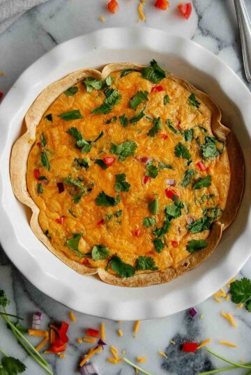 pie plate with tortilla quiche bake on countertop with parsley on top.
