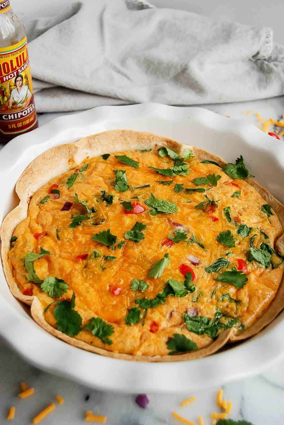 side view of tortilla quiche with hot sauce on the side.