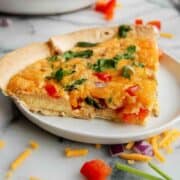 side view of tortilla quiche bake on plate with full quiche on the background.