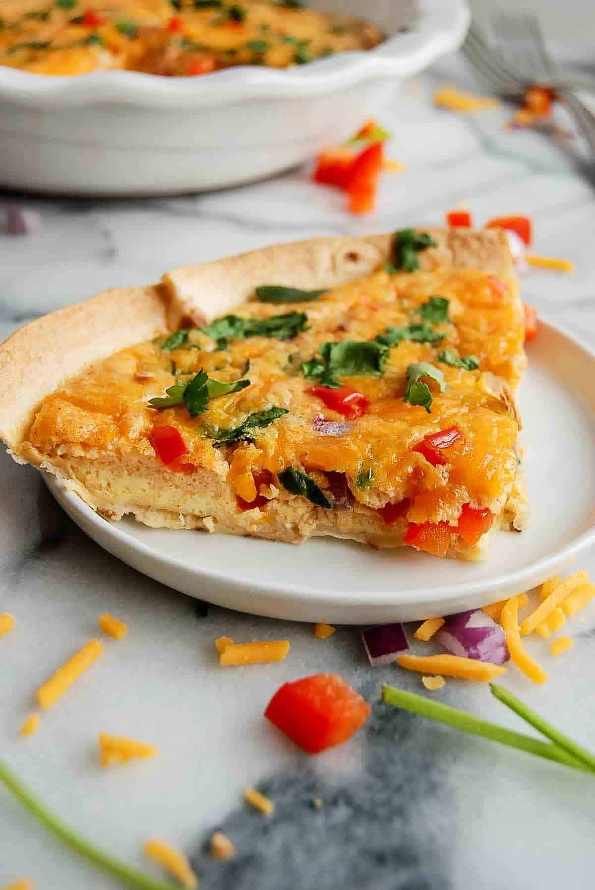 side view of tortilla quiche bake on plate with full quiche on the background.