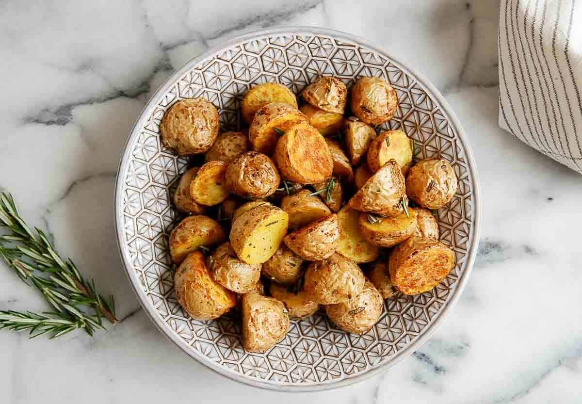 air fryer baby potatoes with garlic and rosemary in bowl on countertop.