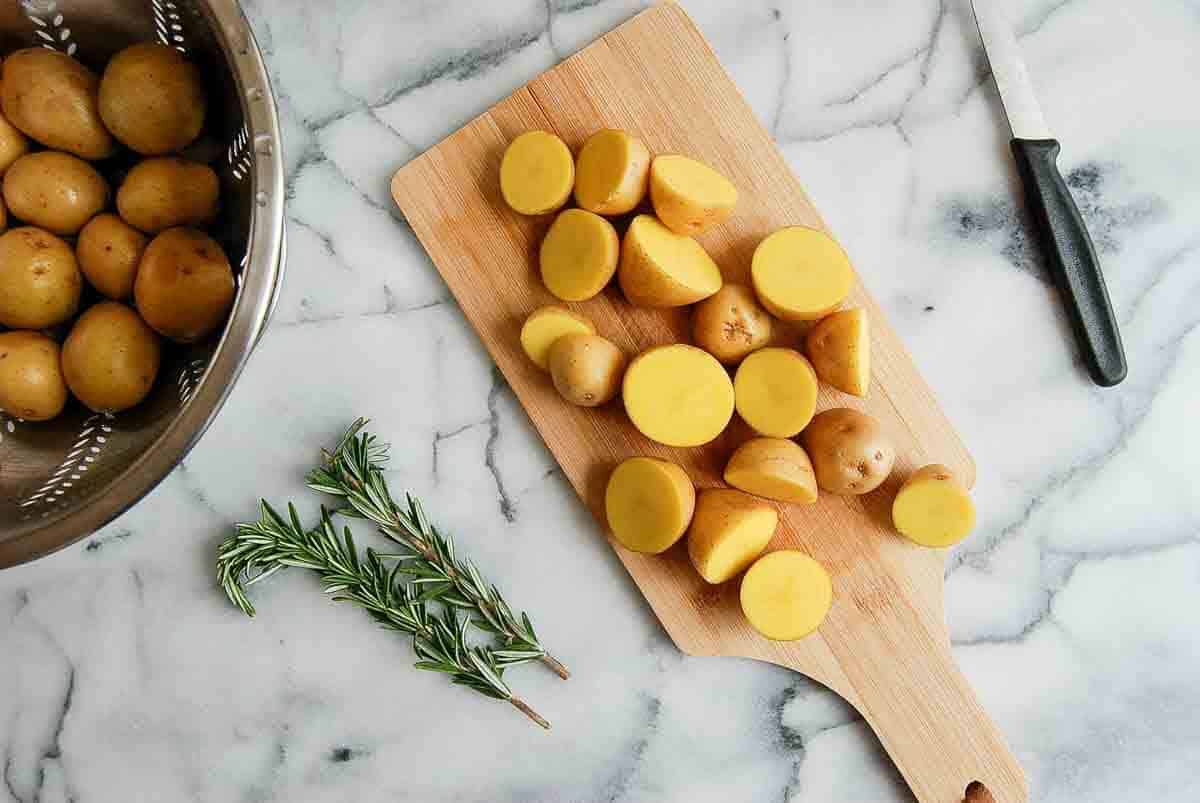 halved baby potatoes on cutting board with rosemary on the side.